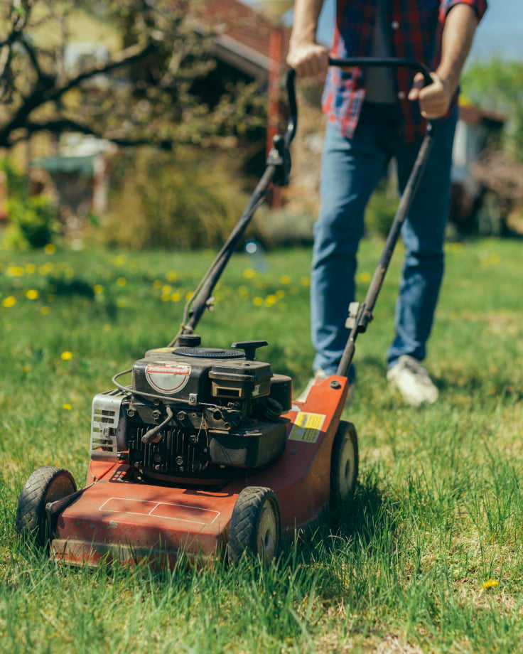 A man pushes an old red gas powered lawn mower.